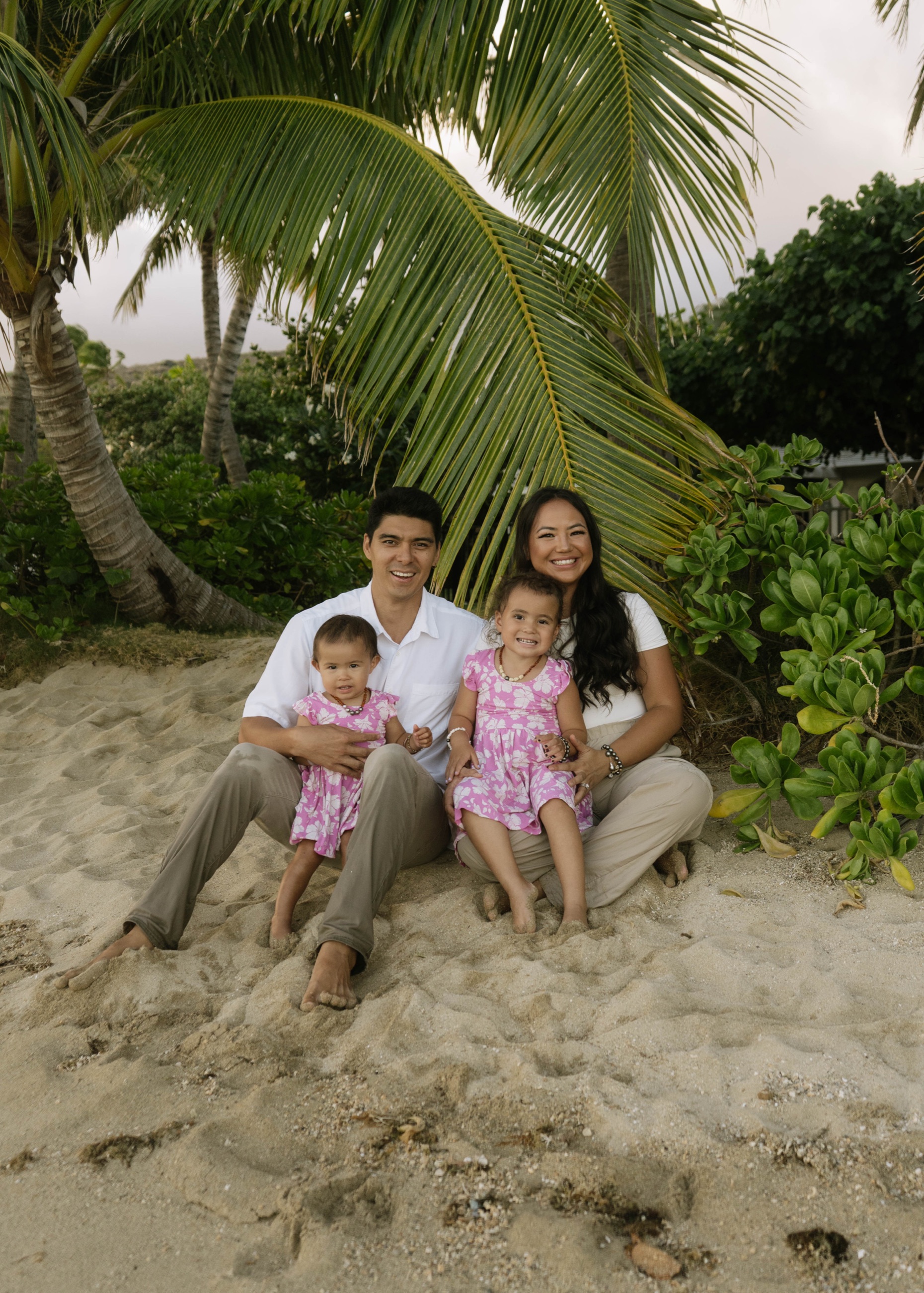 Family of four sitting on the beach under a palm tree