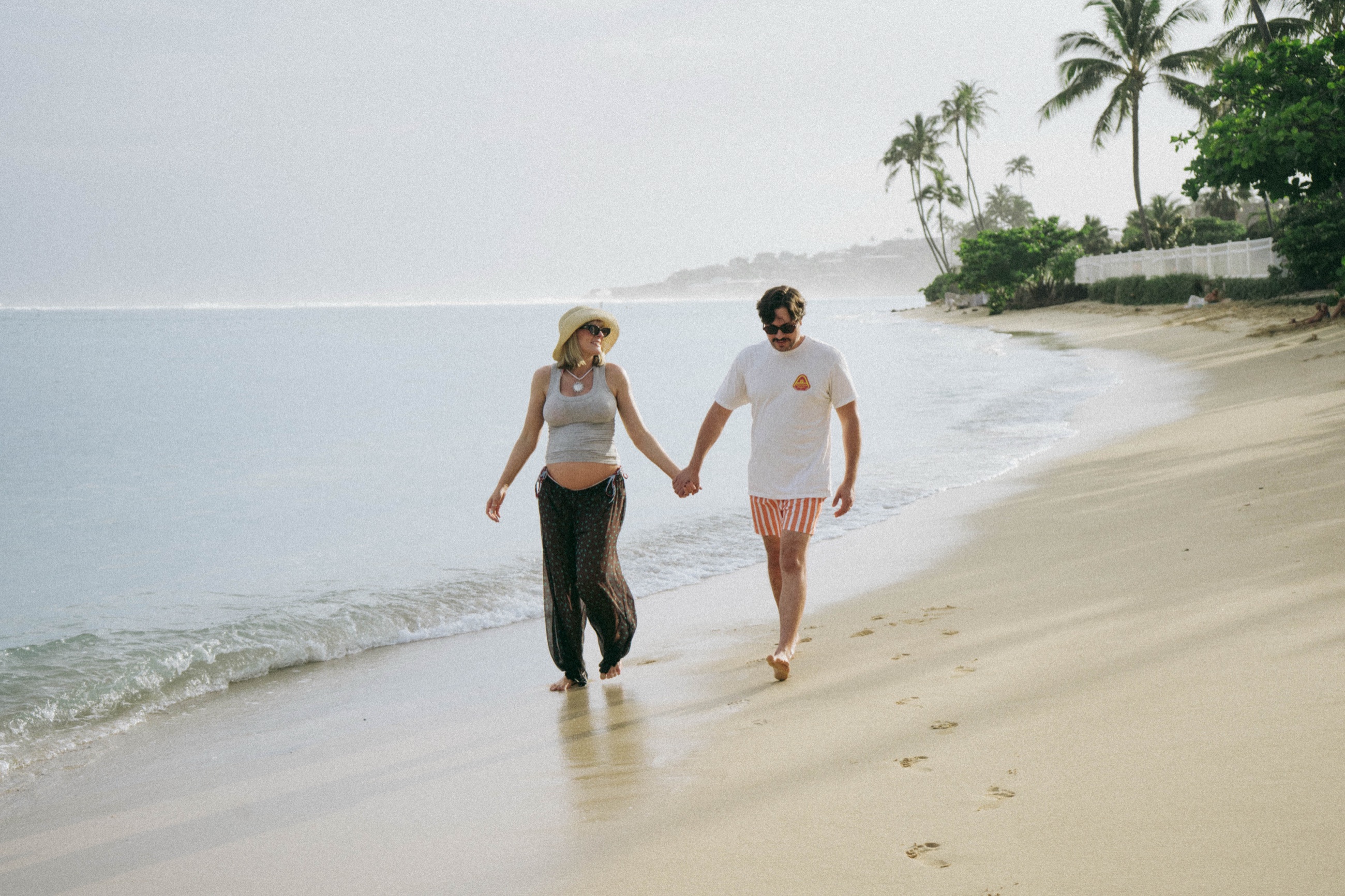 Pregnant couple holding hands while walking on the beach
